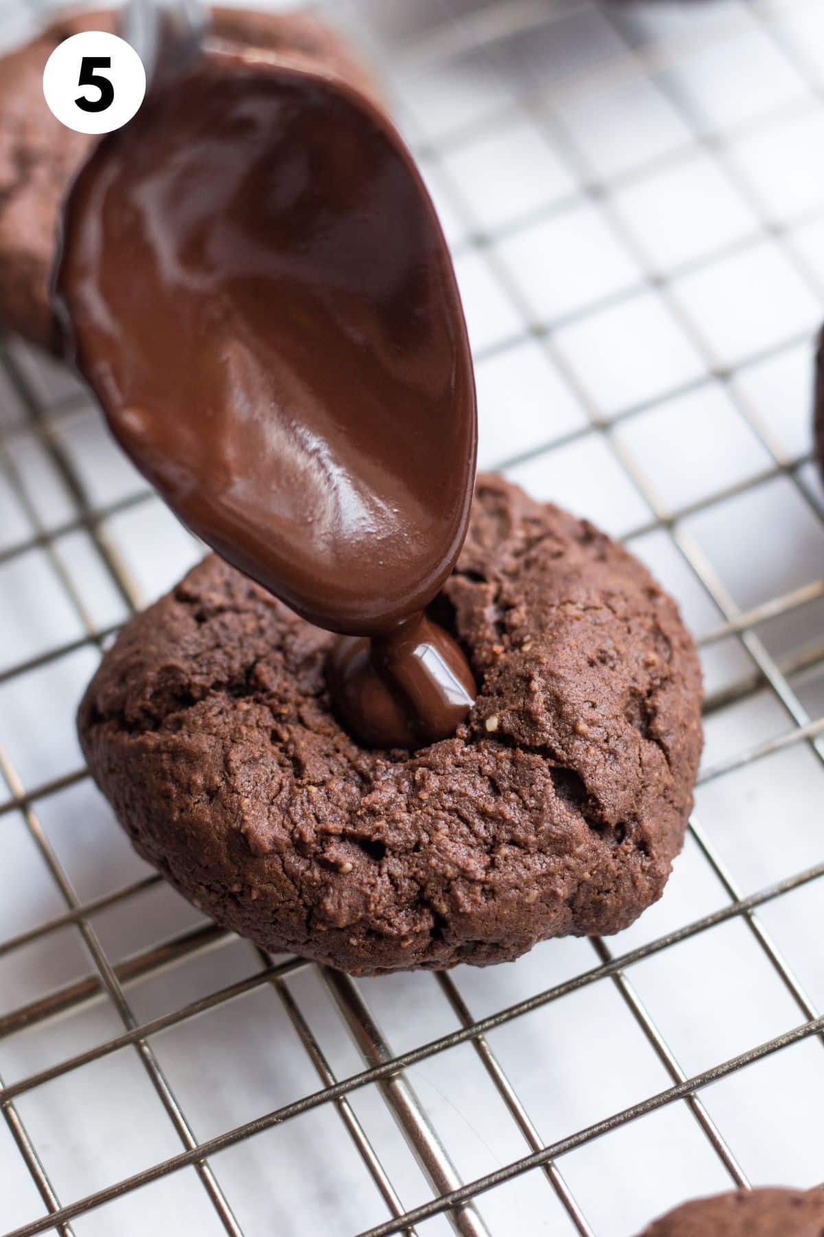 Baked thumbprint cookies being filled with chocolate ganache.