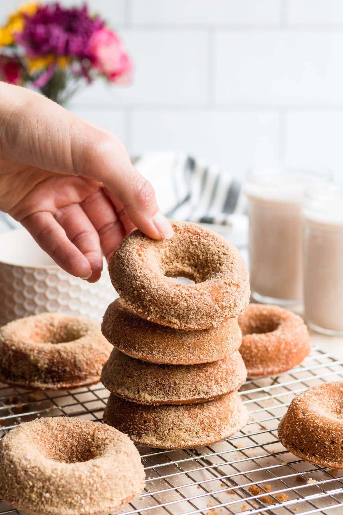 A stack of gingerbread donuts on a cooling rack with a hand taking one off.
