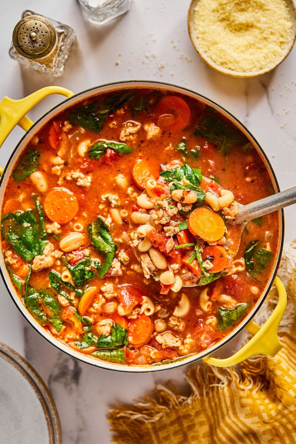 A large pot of healthy pasta fagioli soup on the table with a ladle lifting up a portion.