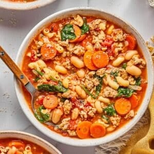 A bowl of healthy pasta e fagioli on the table with a spoon digging in.