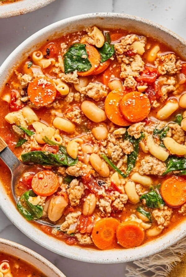 A bowl of healthy pasta e fagioli on the table with a spoon digging in.