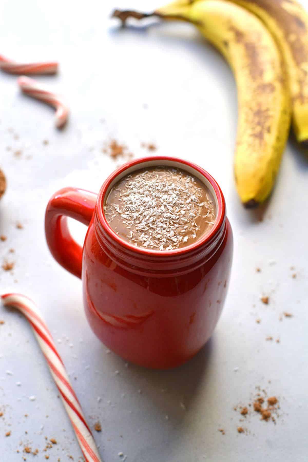 A mug of hot chocolate smoothie on a table with a banana.