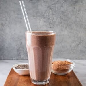 A glass of hot chocolate smoothie on a wooden cutting board.