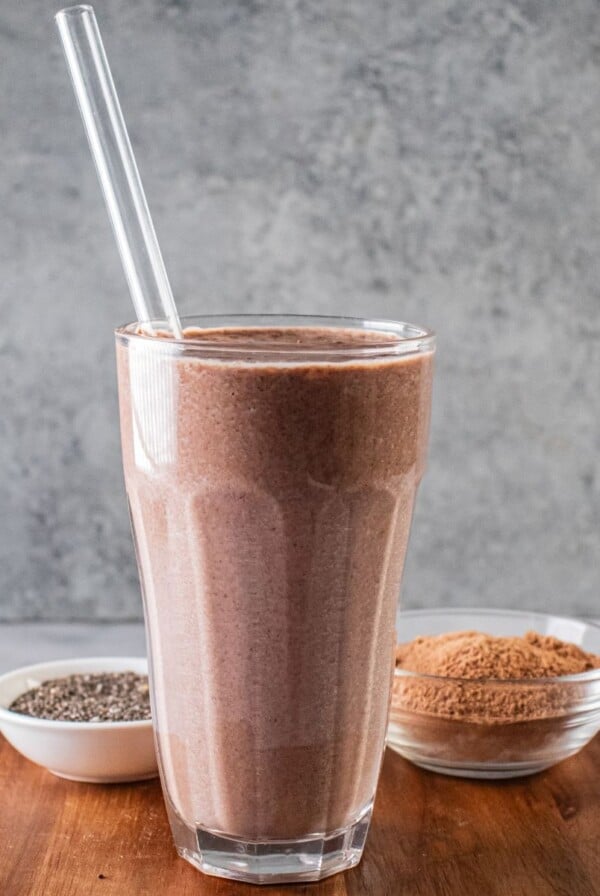 A glass of hot chocolate smoothie on a wooden cutting board.