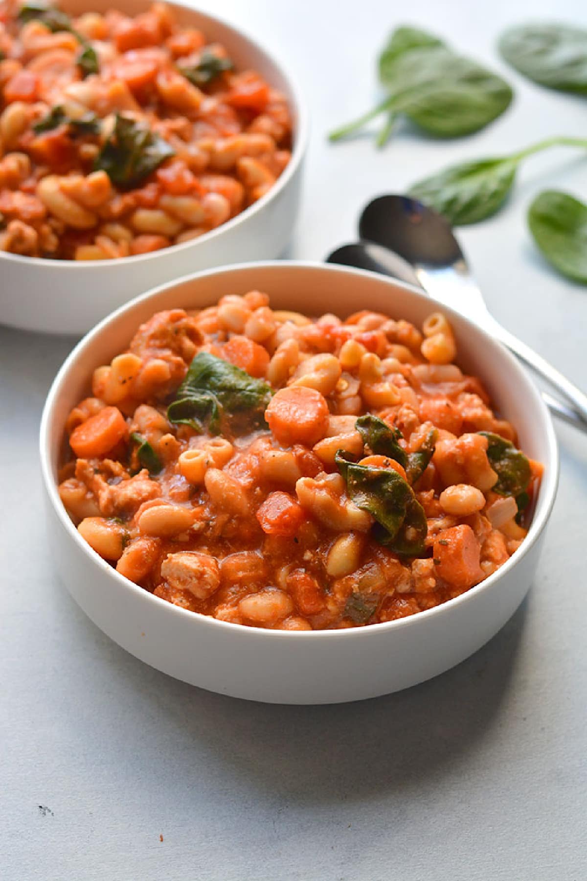 Two bowls of pasta e fagioli in white bowls on a white table.