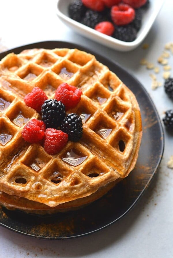 oatmeal waffle on a black plate with blackberries and raspberries on top and maple syrup.