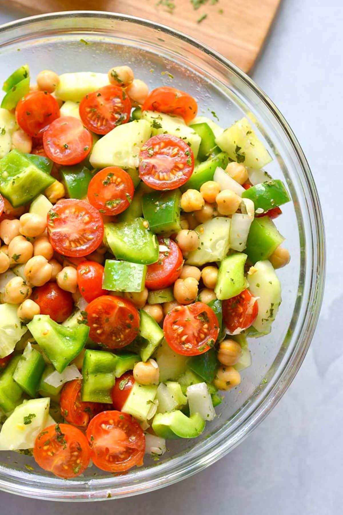 A bowl of chickpea tomato and cucumber salad on a wooden cutting board.