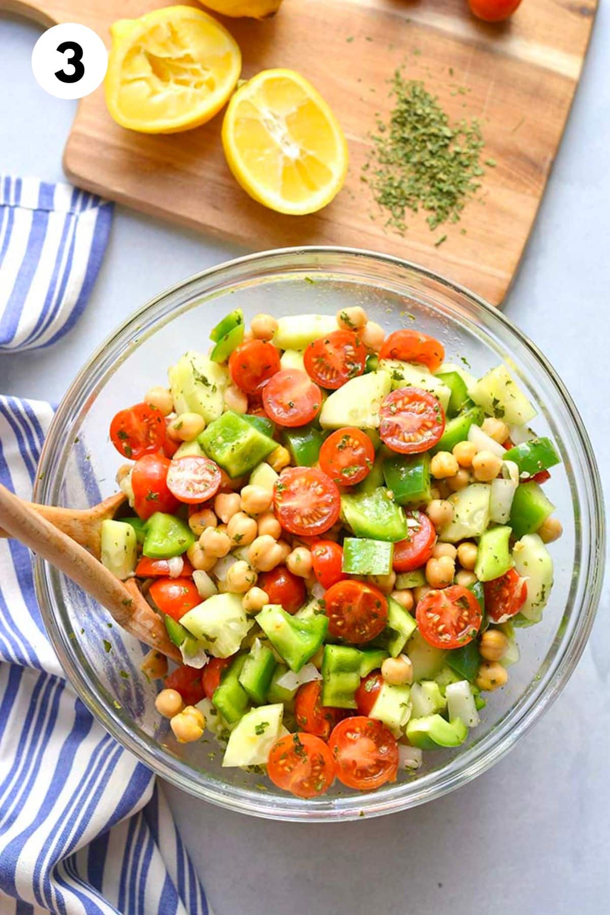 Finished chickpea tomato cucumber salad with a wooden spoon in the bowl.