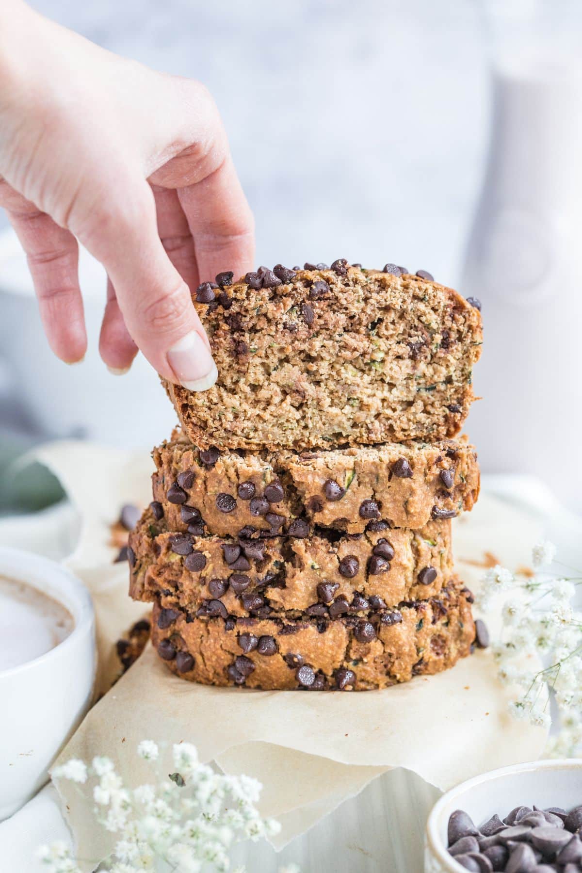 A stack of zucchini bread slices with a hand reaching to pick a slice up from the top. 