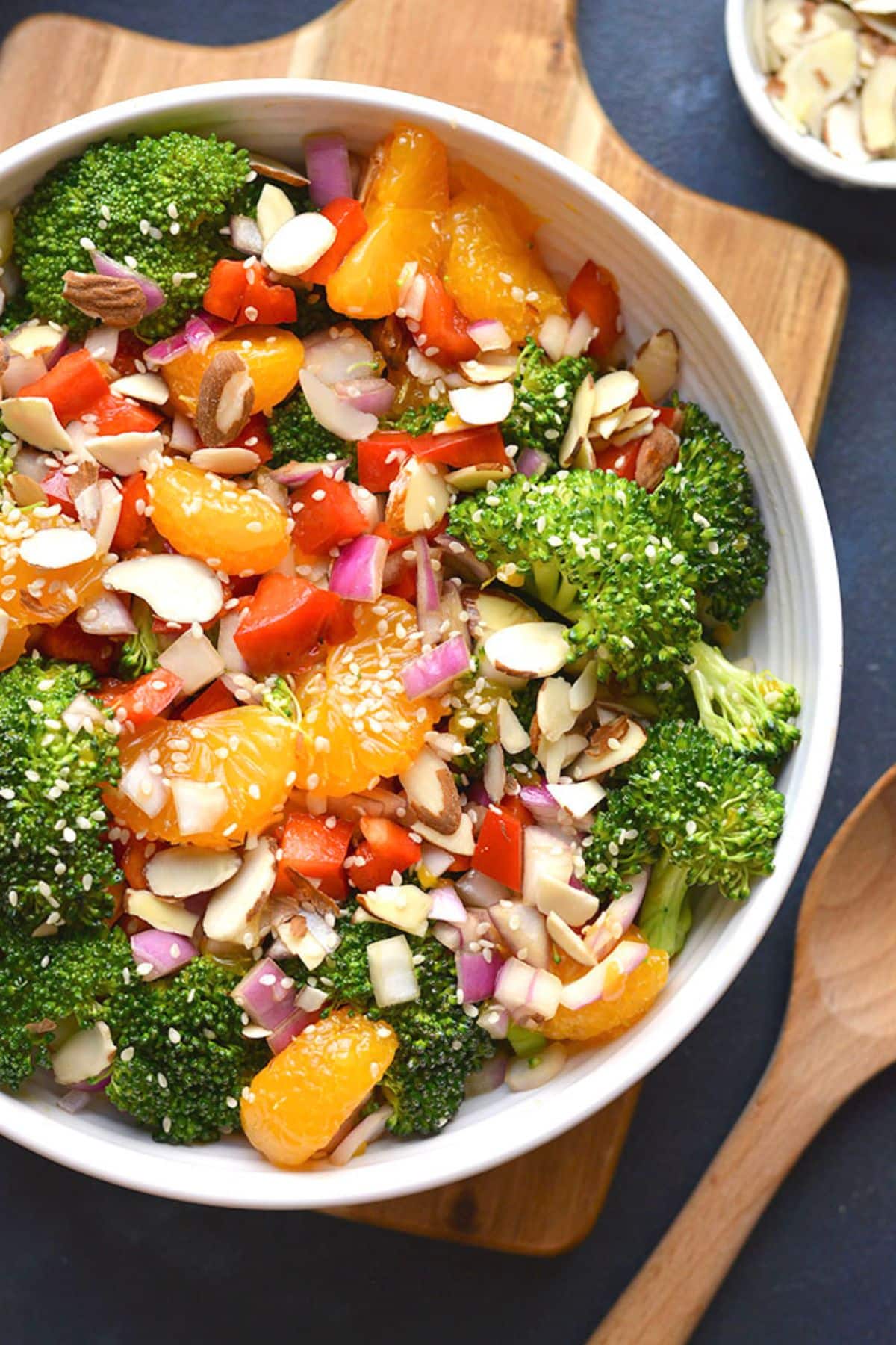 A bowl of Asian broccoli salad with a wooden spoon resting on the side.