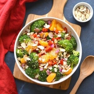 Asian broccoli salad in a bowl next to a wooden spoon and bowl of almonds.