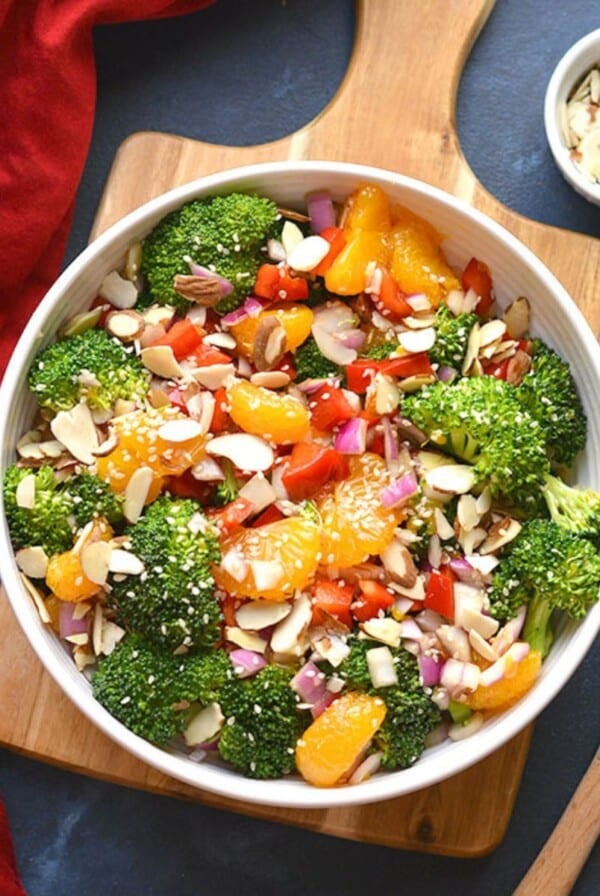 Asian broccoli salad in a bowl next to a wooden spoon and bowl of almonds.