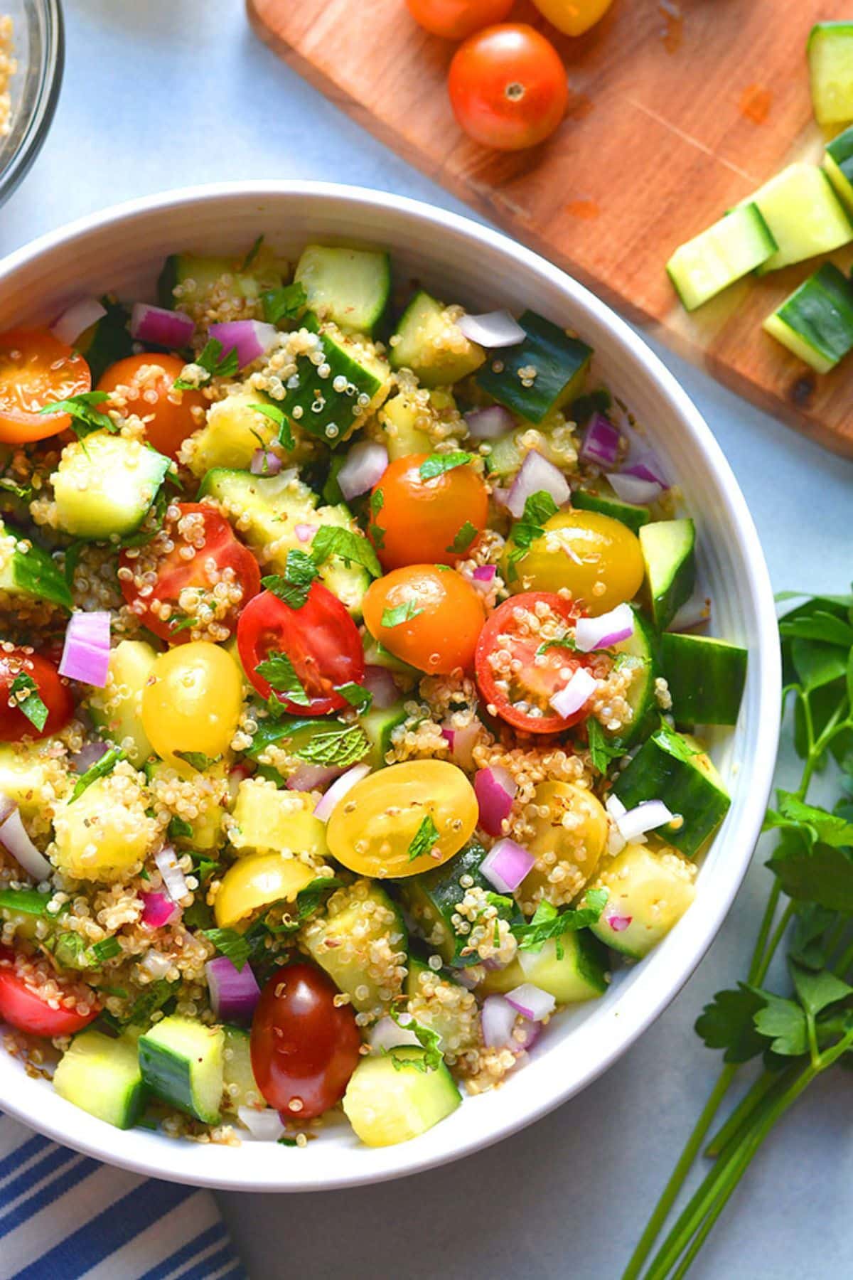 A bowl of healthy tabbouleh salad with quinoa on a table with some cucumber and grape tomatoes to the side.