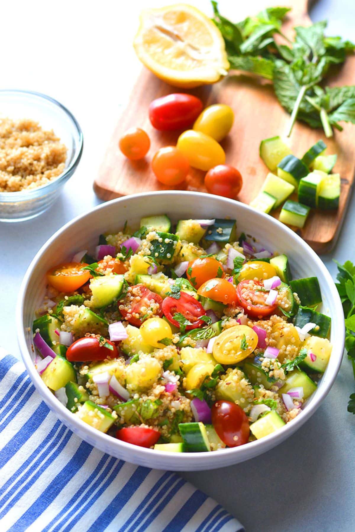 Healthy quinoa tabbouleh salad in a bowl with chopped vegetables and a bowl of quinoa to the side.
