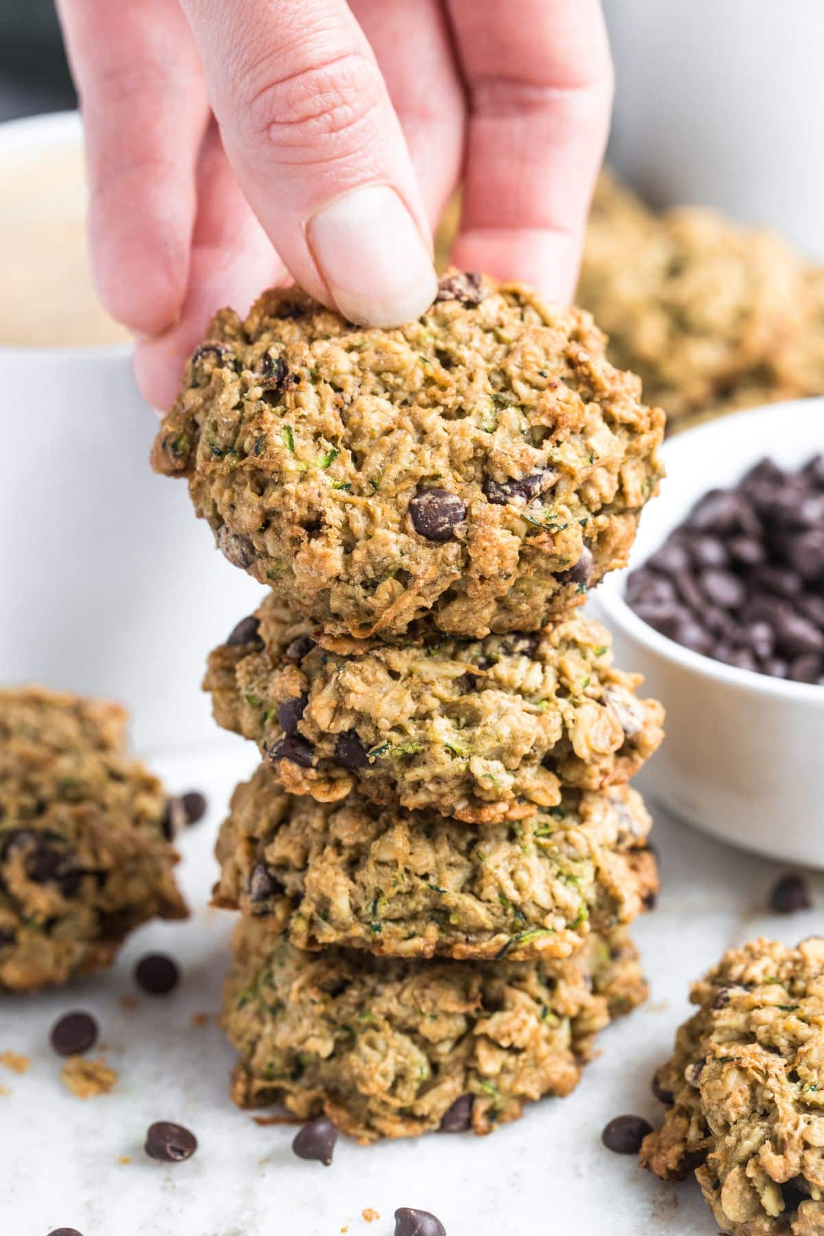 A stack of zucchini chocolate chip cookies with a hand placing one on top.