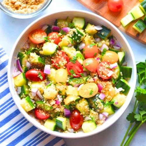 A white bowl of quinoa tabbouleh next to a blue and white tea towel.