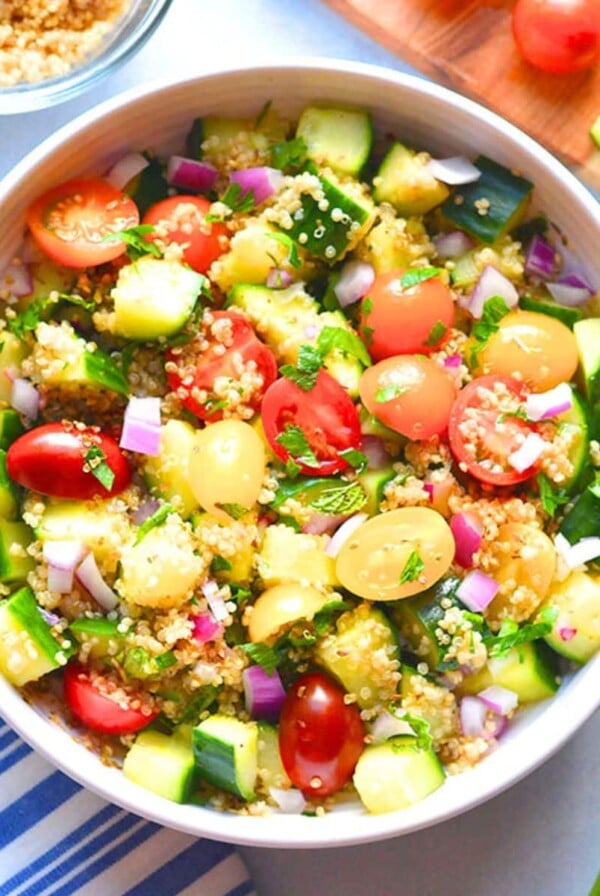 A white bowl of quinoa tabbouleh next to a blue and white tea towel.