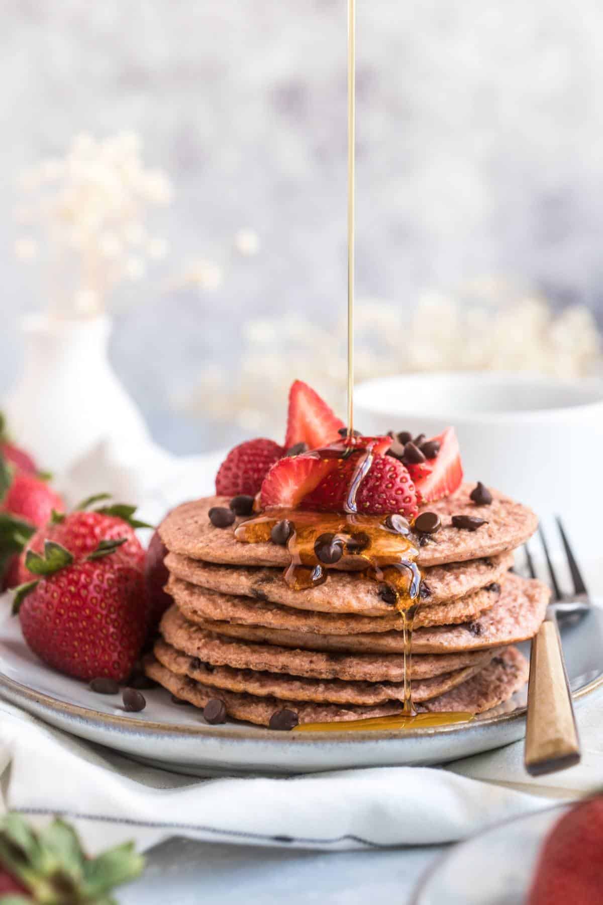 A stack of strawberry pancakes with a drizzle of syrup on top.