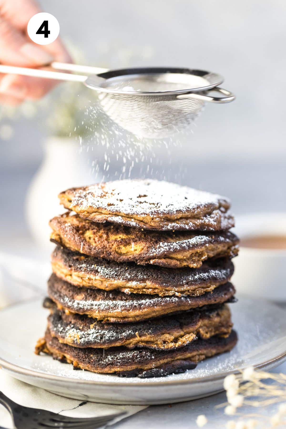 Powdered sugar being sprinkled onto a stack of pumpkin pancakes.