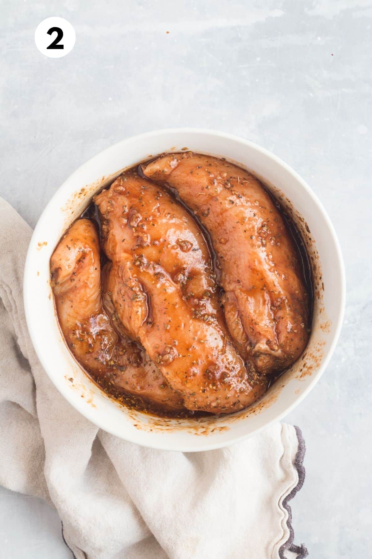 Raw chicken covered in marinade in a bowl.