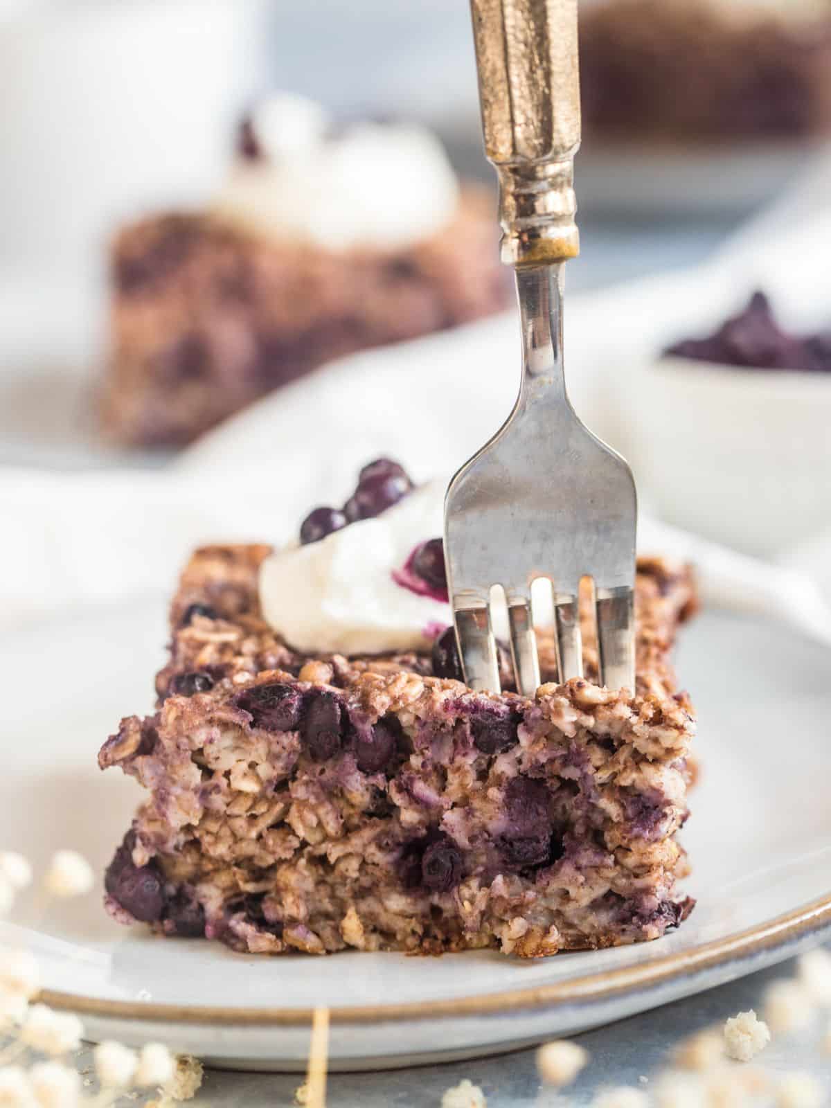 A serving of healthy blueberry baked oatmeal on a plate with a fork sticking into it for a bite. 