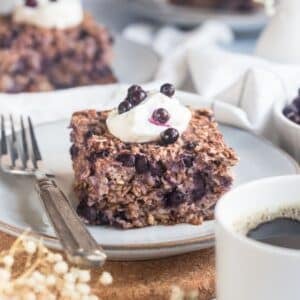 A serving of healthy baked oatmeal with blueberries on a plate topped with Greek yogurt and more blueberries.