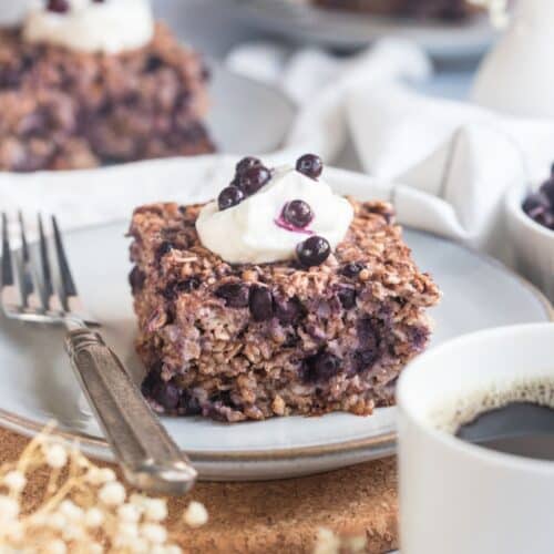 A serving of healthy baked oatmeal with blueberries on a plate topped with Greek yogurt and more blueberries.