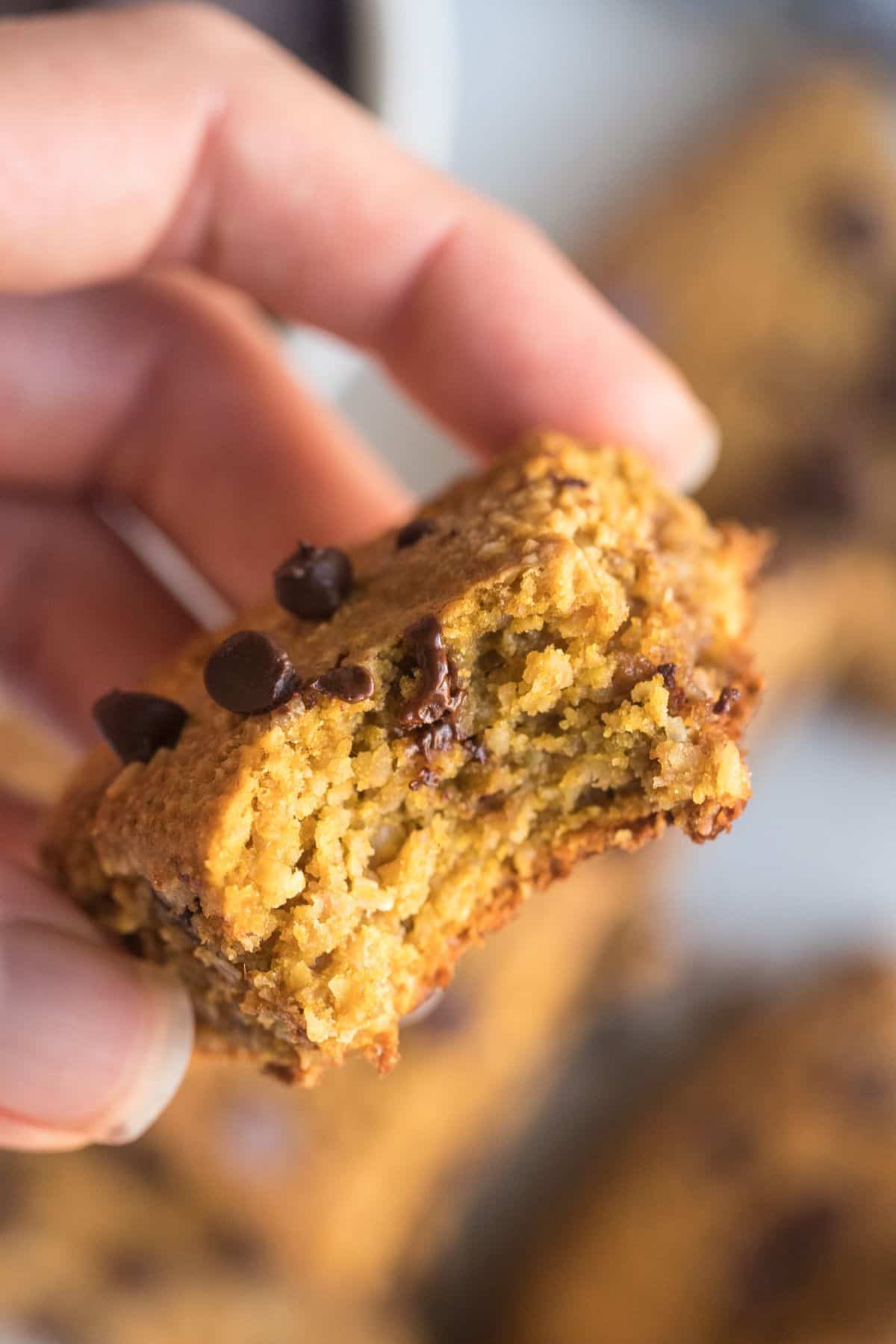 A hand holding up a pumpkin scone with a bite taken out of it.
