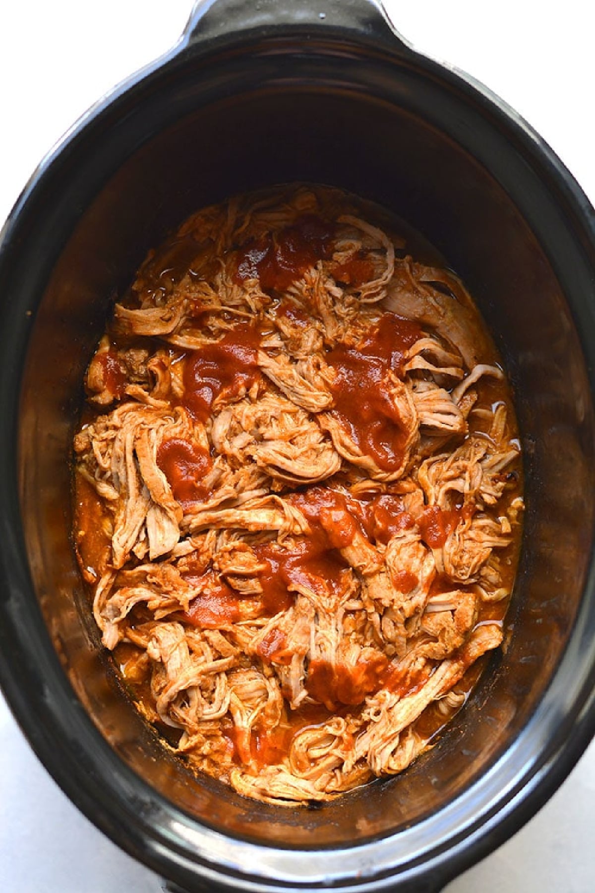 cooked shredded pork with bbq sauce on top in a slow cooker.