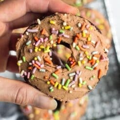 A hand holding up a chocolate protein donut with sprinkles.