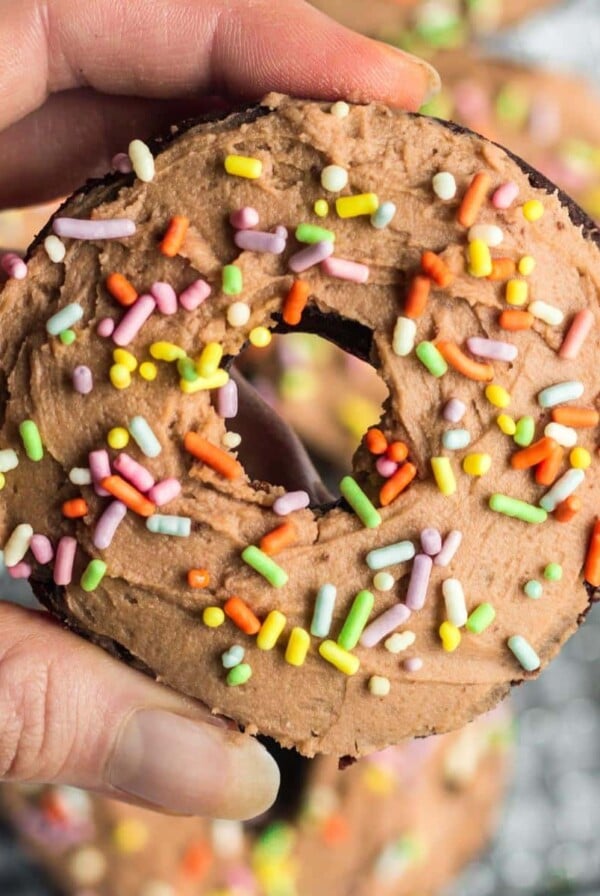 A hand holding up a chocolate protein donut with sprinkles.