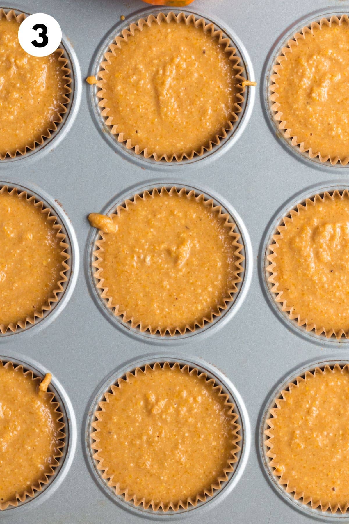 Pumpkin cornbread muffin batter in a muffin tin.