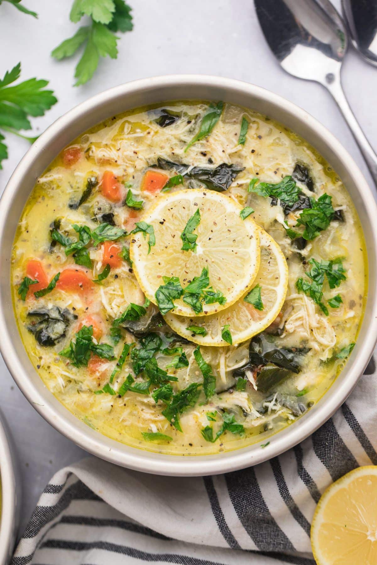 A bowl of healthy Greek Lemon Chicken Soup on the table with a gray and white towel and lemons.