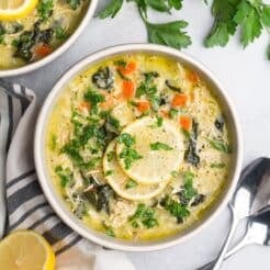A bowl of greek lemon chicken soup on the table topped with lemon slices and herbs.