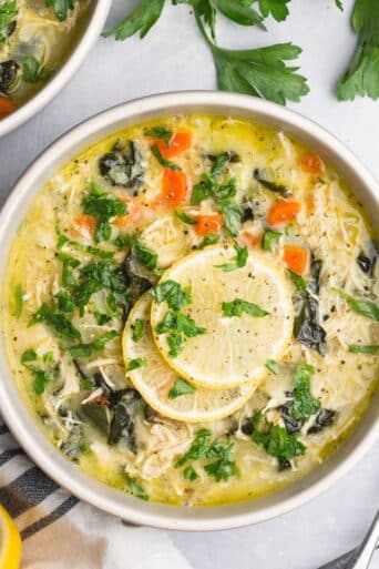 A bowl of greek lemon chicken soup on the table topped with lemon slices and herbs.