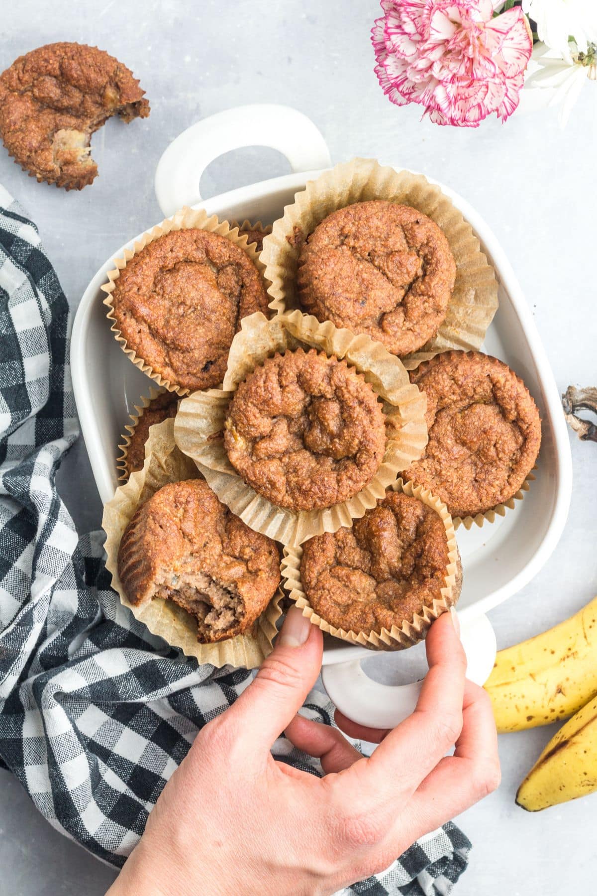 A hand reaching in to grab a gluten-free banana muffin from a platter of more. 