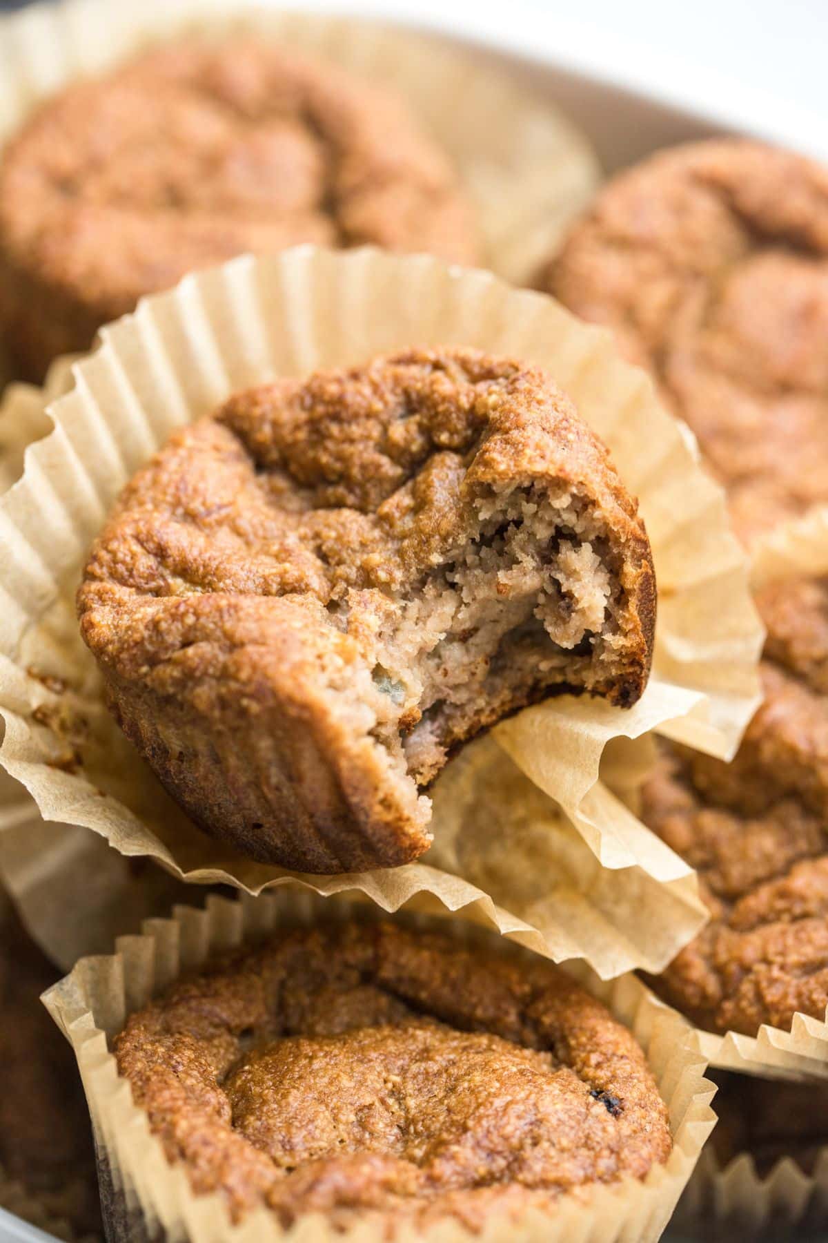  A pile of banana muffins with almond flour and a bite missing from one on top. 
