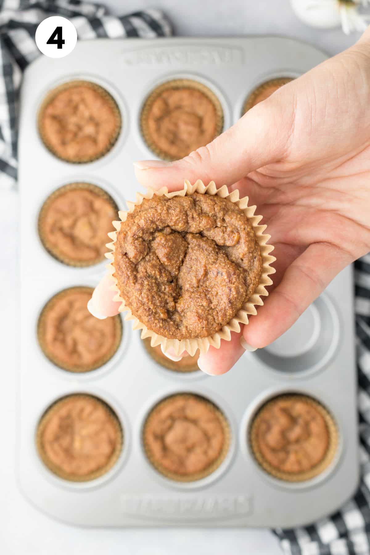 A hand holding up a baked almond flour banana muffin over the pan of more.