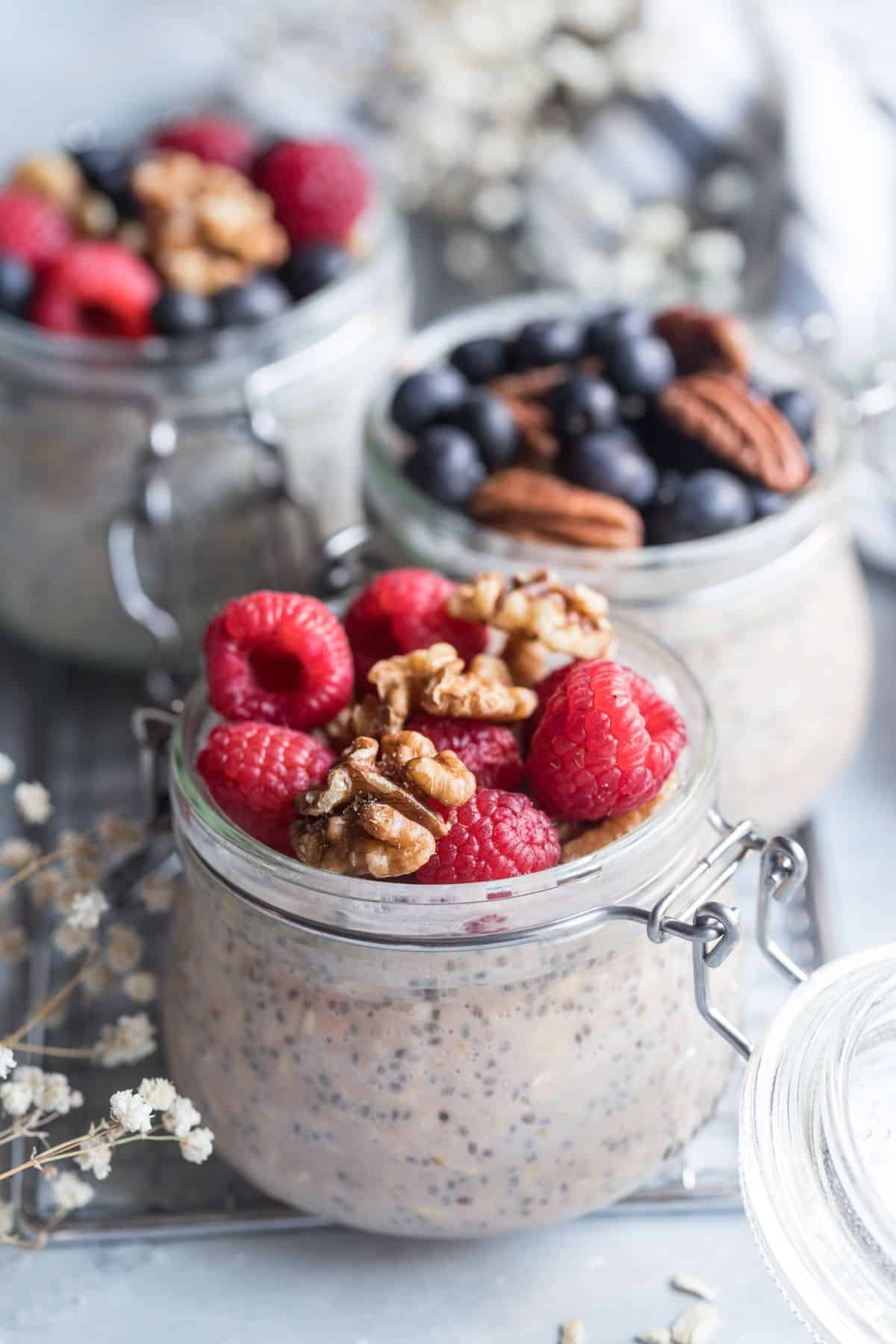 Three jars of protein overnight oats on the table with fresh berries and nuts.