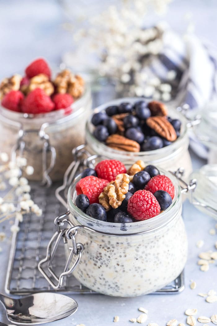 Jars of overnight protein oats on a wire rack on the table topped with raspberries and blueberries.