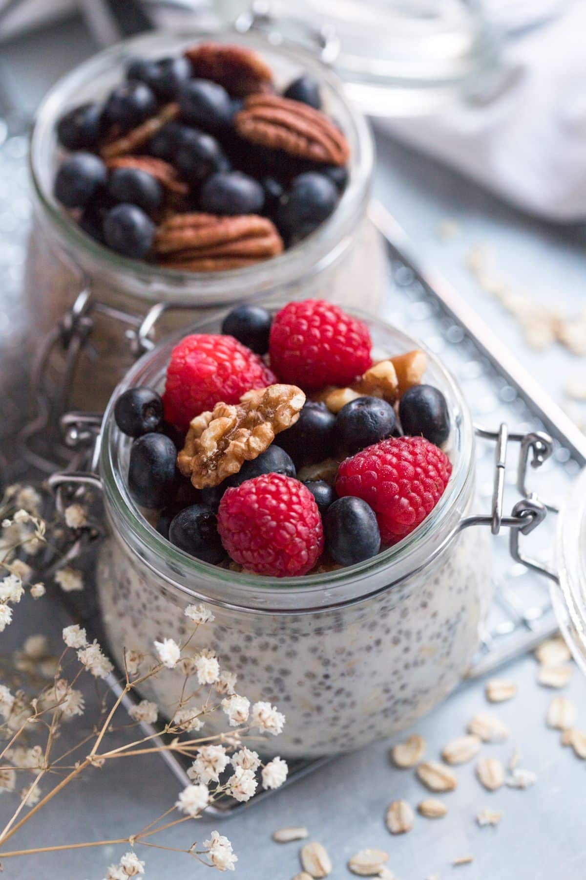 Two jars of overnight oats with protein powder on the table topped with fresh berries and nuts.