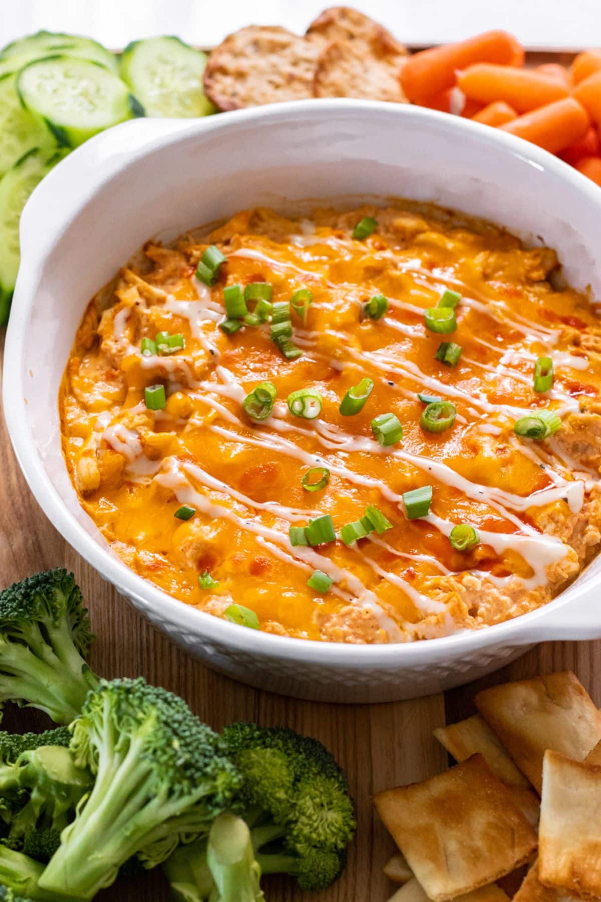 Healthy Buffalo Chicken Dip in a white casserole dish on the table wiht veggies in the background.