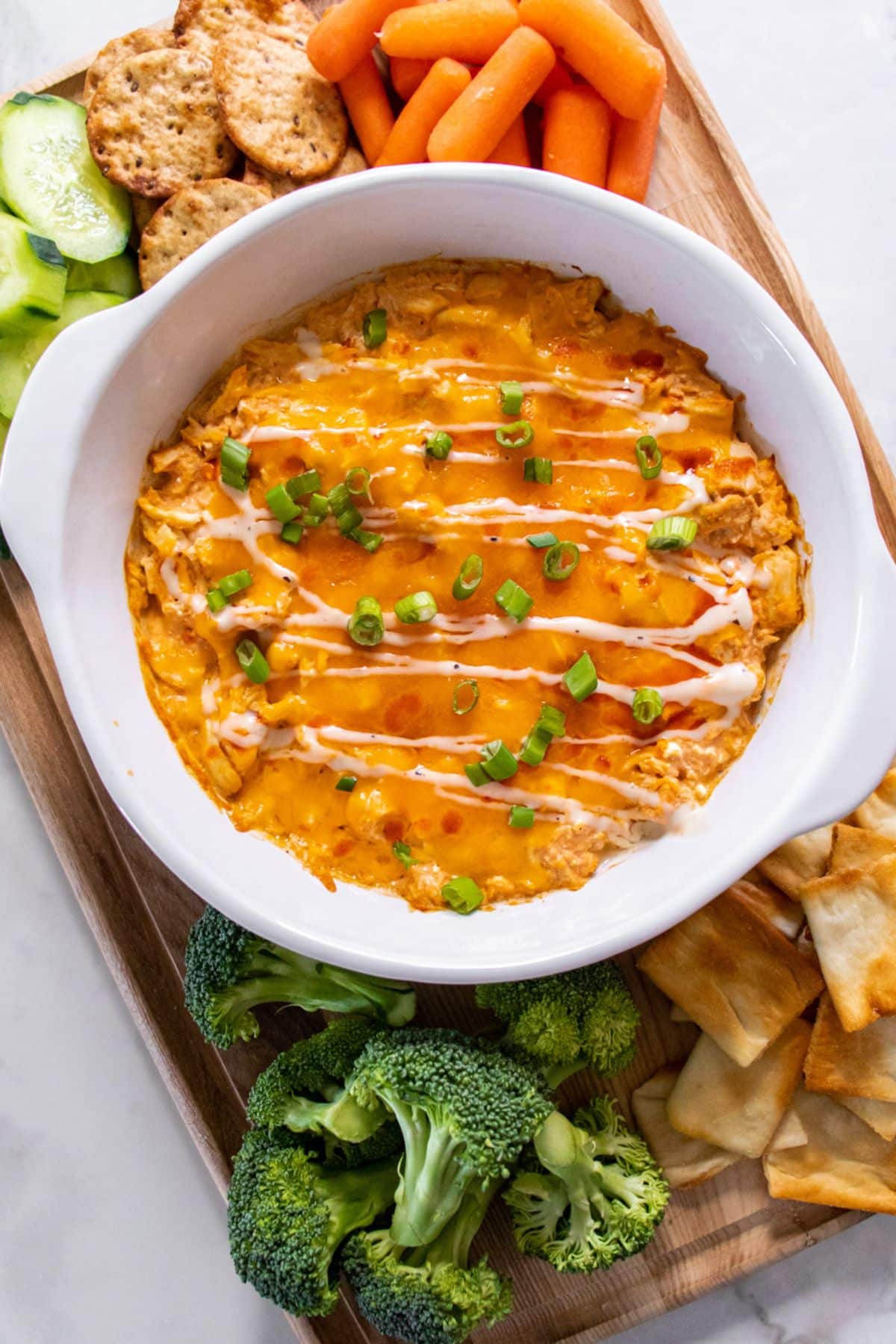 A dish of healthy chicken wing dip on a cutting board surrounded by dippers.