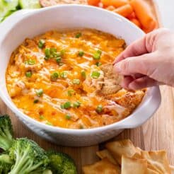A hand dipping a cracker into a healthier buffalo chicken dip with cottage cheese.