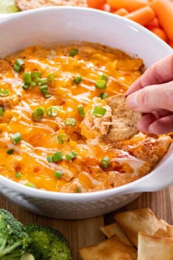 A hand dipping a cracker into a healthier buffalo chicken dip with cottage cheese.