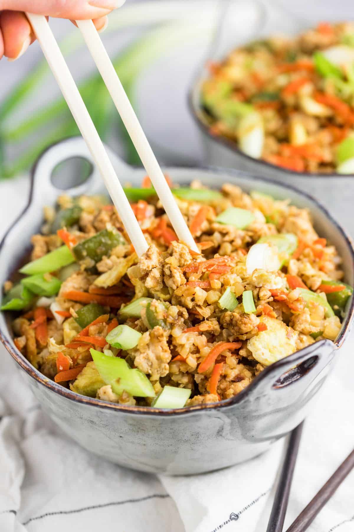 A bowl of healthy fried rice with chopsticks reaching to grab a bite.