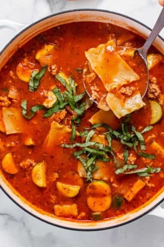 A pot of healthy lasagna soup on the table with a ladle lifting up a serving.