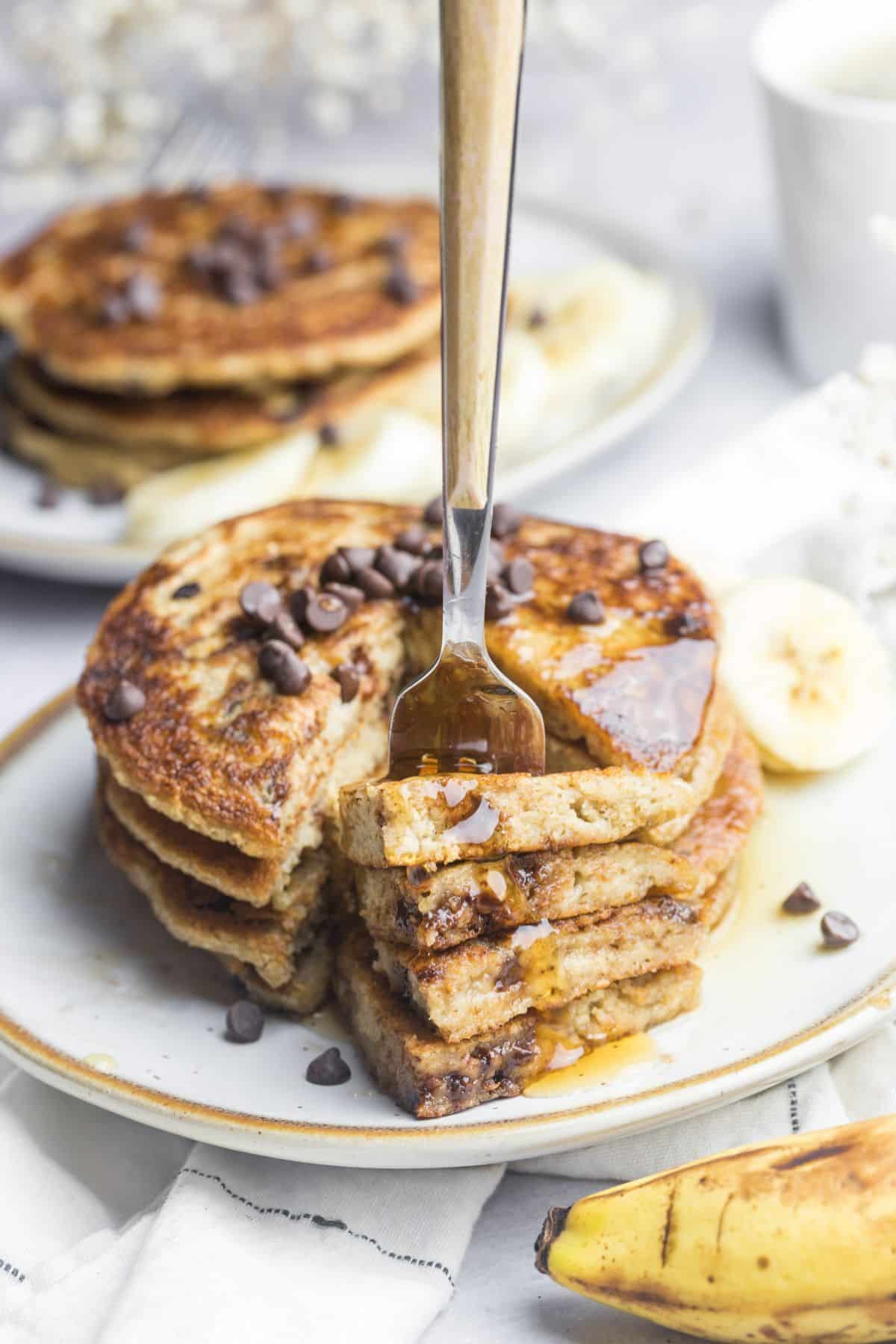 A fork picking up a bite of banana chocolate chip pancakes cut from a stack. 