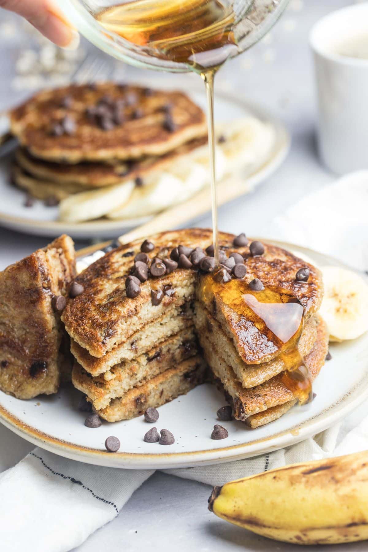 A stack of banana chocolate chip pancakes with syrup drizzling over the top and a bite missing.
