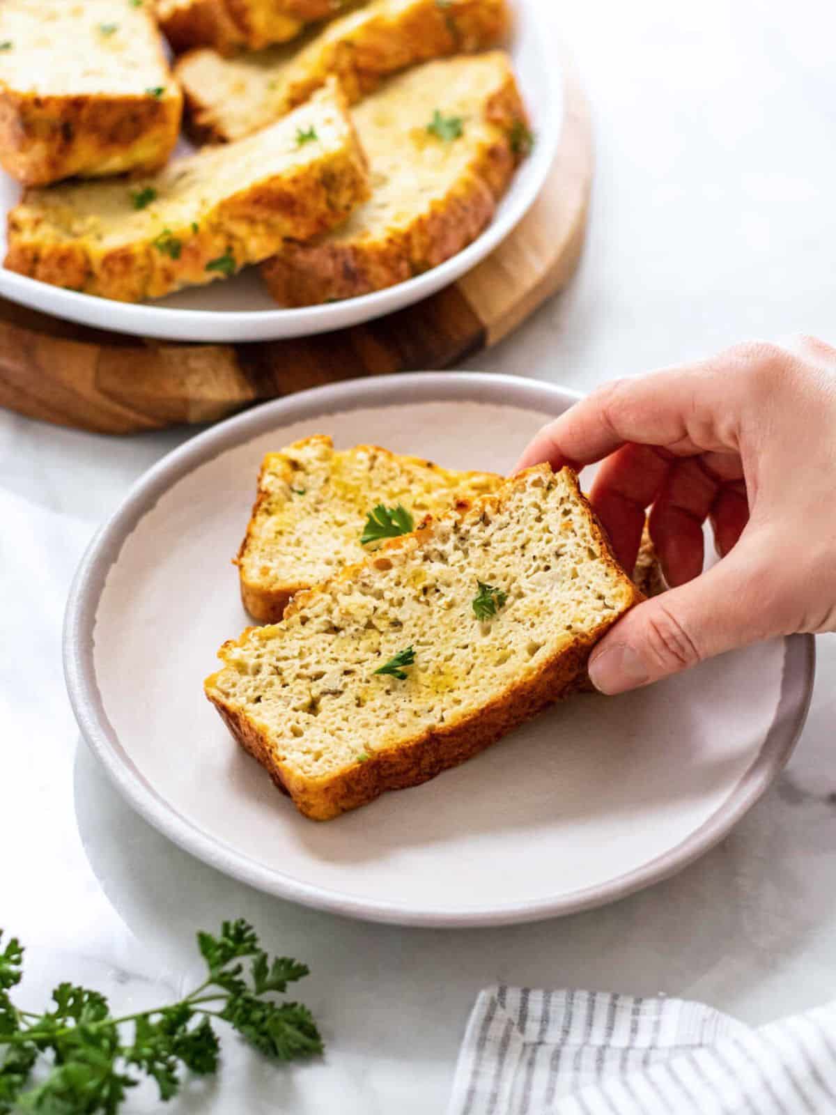 A hand reaching to pick up a piece of cauliflower bread from a plate. 
